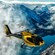 A helicopter soars above clouds, mountains and a lake